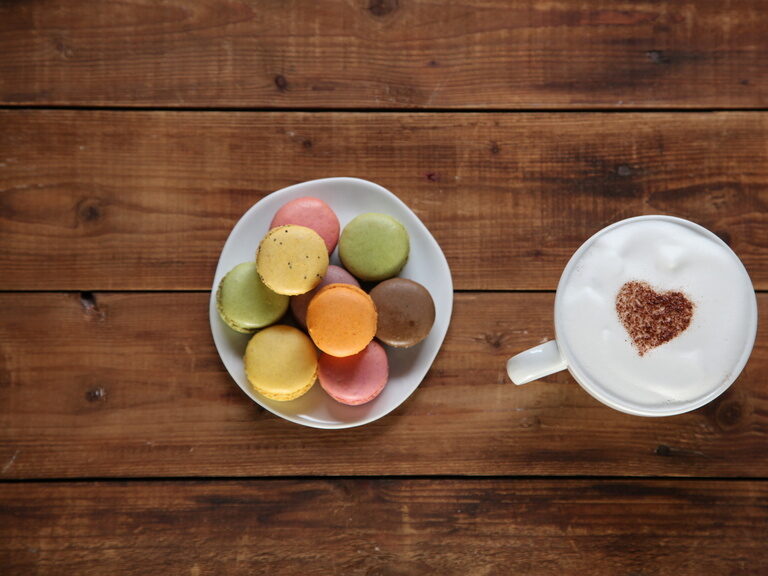 Eine Tasse Kaffee neben einem Teller mit einem Dessert auf einem Holztisch.
